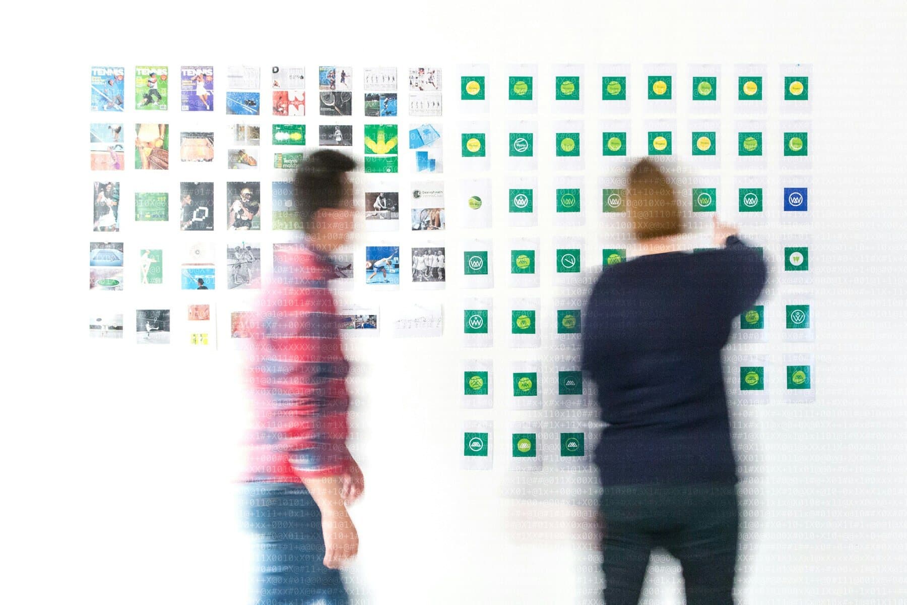Dos personas organizando pantallas impresas en una pared blanca