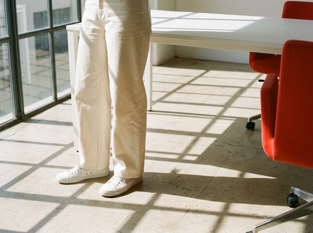 Persona de pie en un estudio luminoso con una mesa blanca y sillas rojas